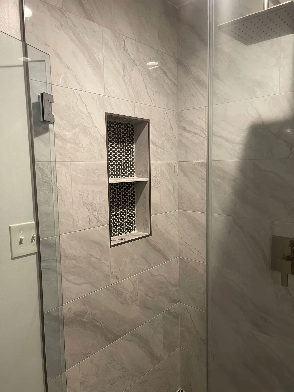 Modern marble tiled shower with glass door and niche